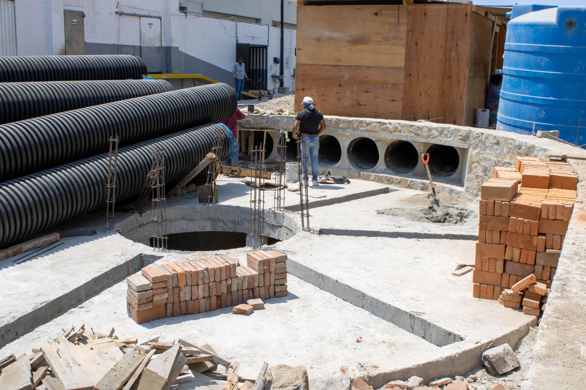 Worker backfilling a large black polyethylene underground water tank